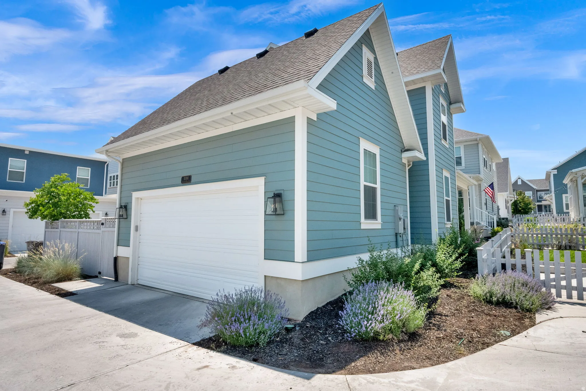 Blue horizontal siding exterior with white trim, a white picket fence, and a landscaped bed with mature plantings