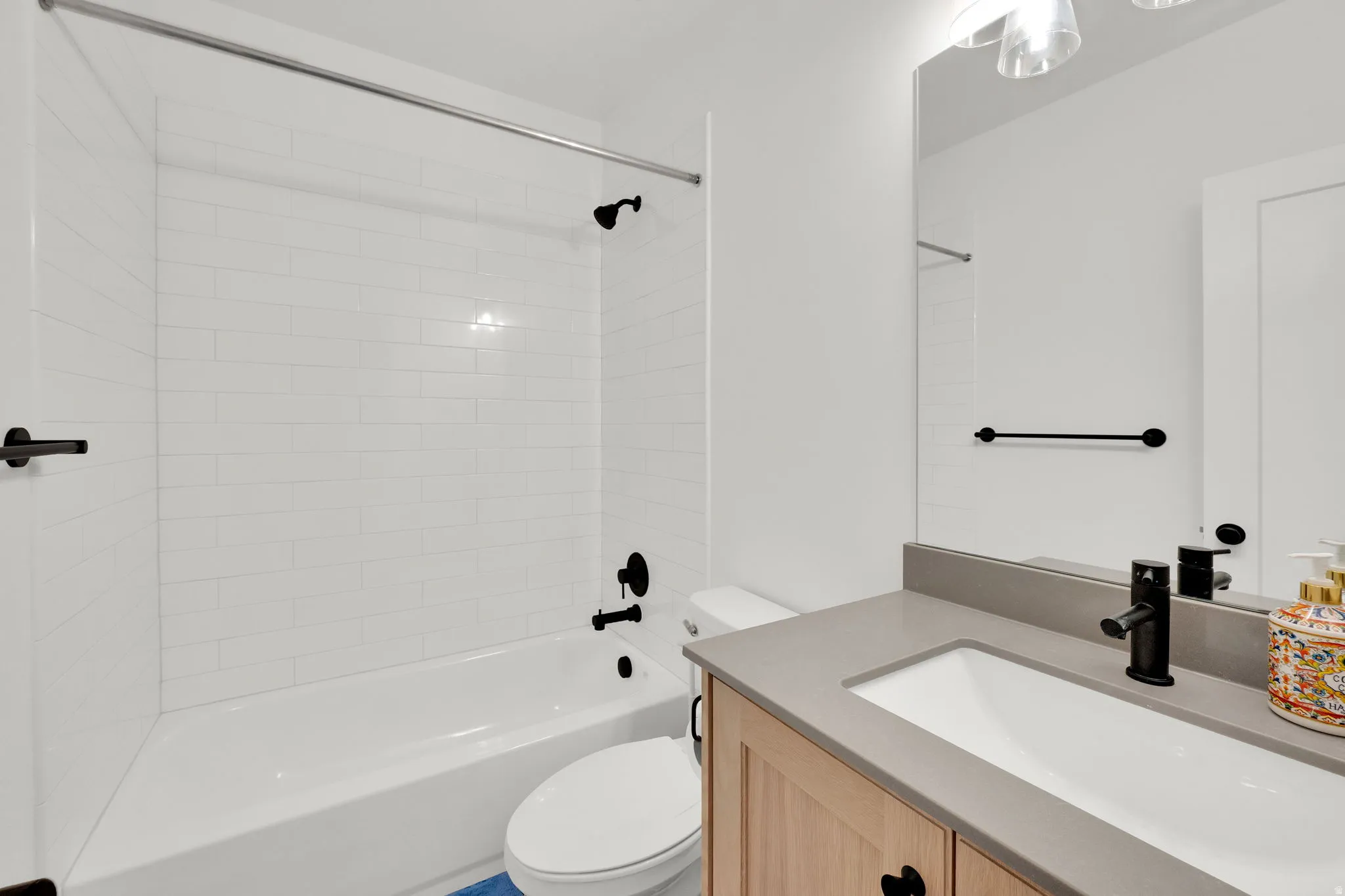 Bathroom featuring a white bathtub with subway tile surround, a vanity with an integrated sink and light-toned wood cabinetry, and matte black fixtures