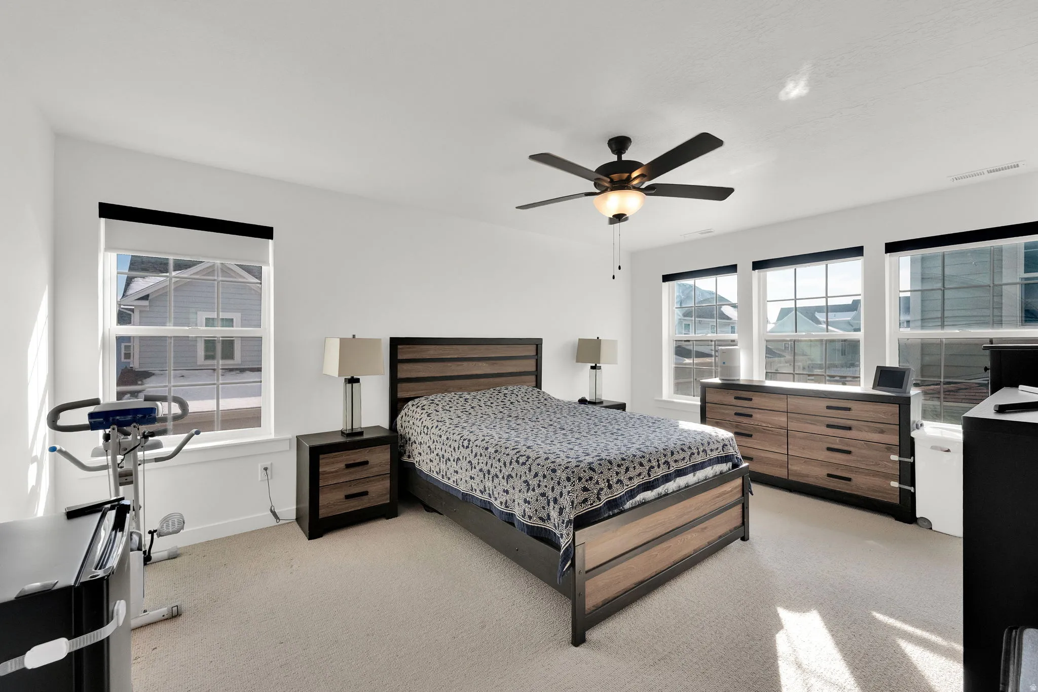 Carpeted room with multiple windows, a ceiling fan with integrated lighting, and white walls