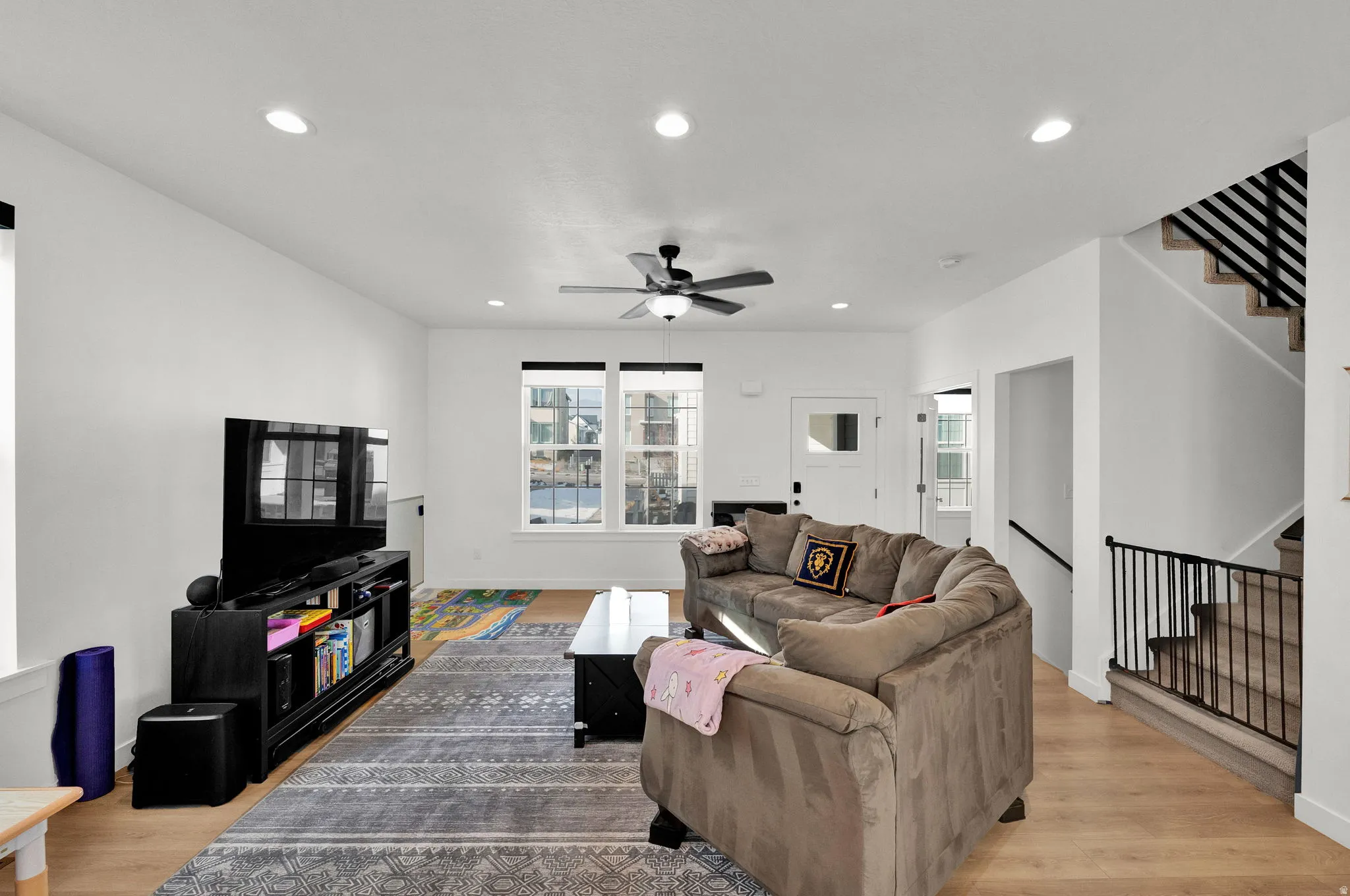 Recessed lighting, wood-finish flooring, ceiling fan, and staircase with metal railings