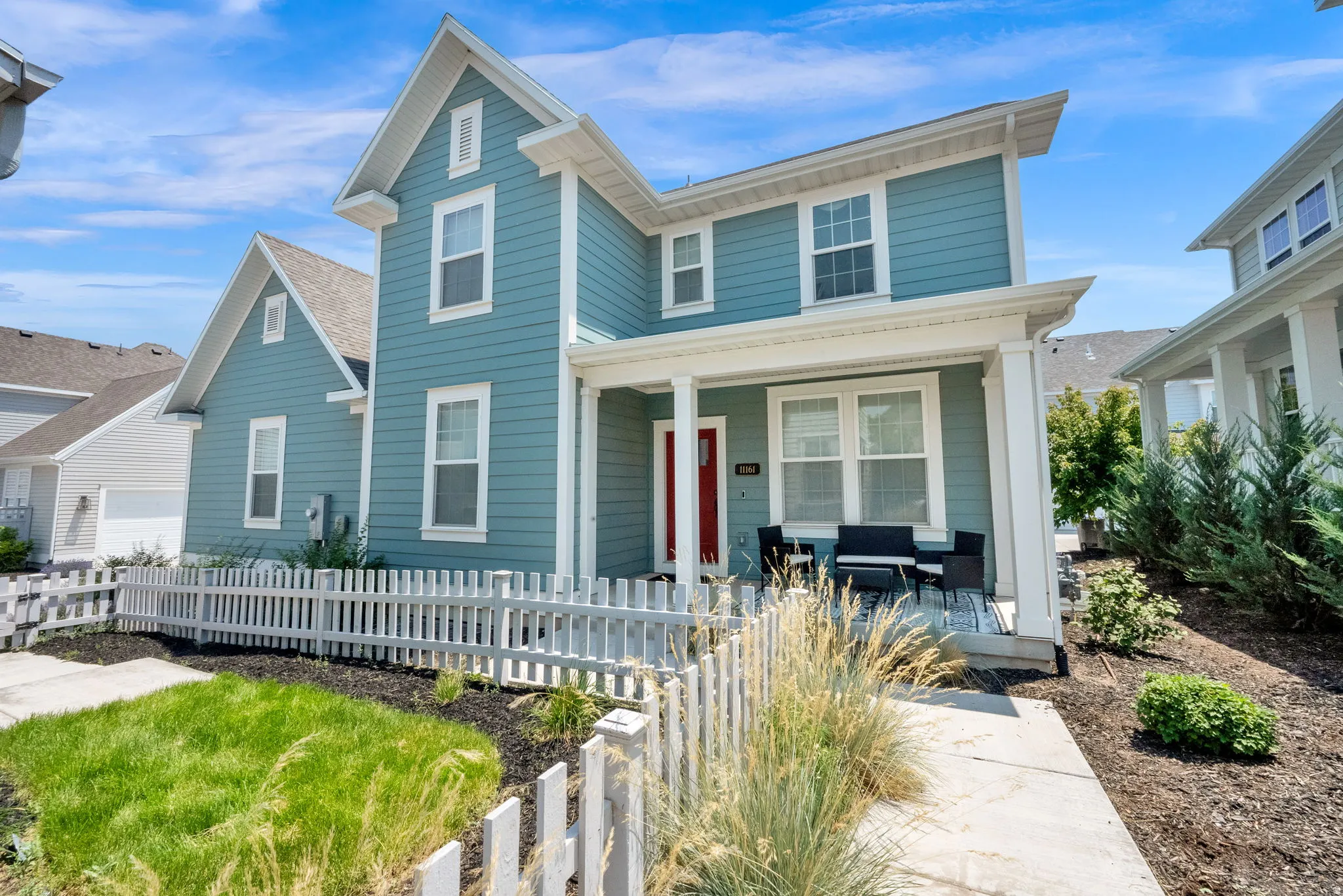 Two-story residential structure featuring blue siding, white trim, a covered front porch, a red entry door, and a white picket fence
