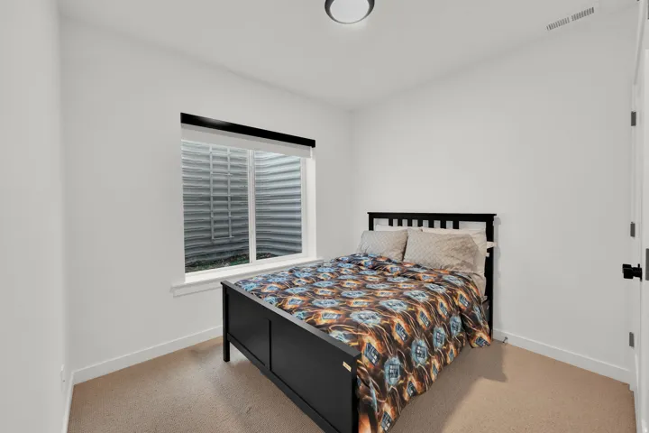 Window with roller blind and exterior window well, light neutral wall paint, and ceiling-mounted flush light fixture