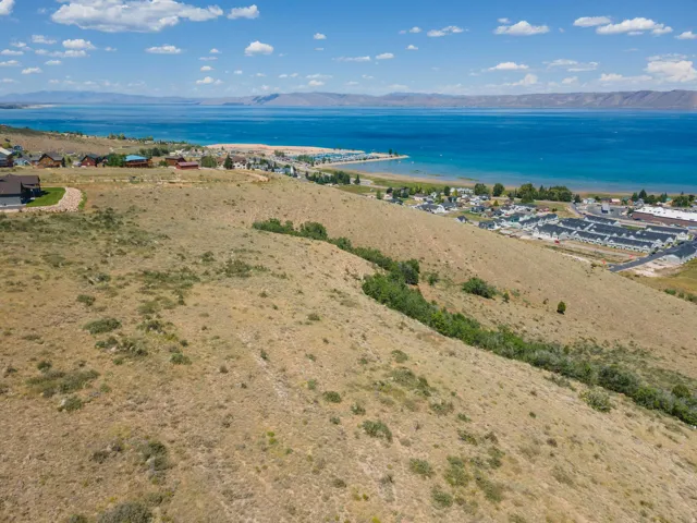 Expansive sloped terrain overlooking a large body of water, with distant mountains under a blue sky with white clouds