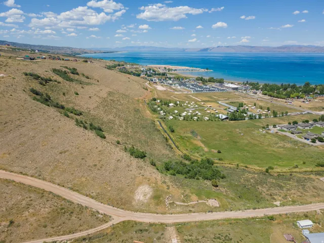 Expansive land parcel featuring natural terrain, a clear blue body of water, and distant low-rise structures