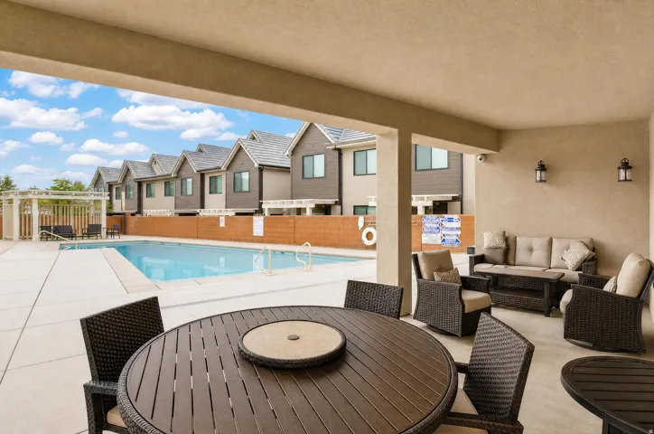 Covered patio offering an outdoor living space, with a pool and multiple residential structures in the background