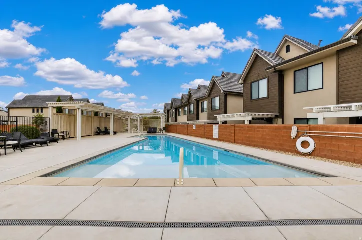 Outdoor swimming pool with integrated sun ledge, surrounded by concrete decking and multiple pergolas