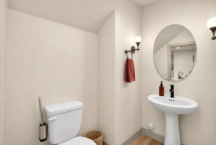 Pedestal sink with black faucet, oval mirror, and wall-mounted sconce lighting
