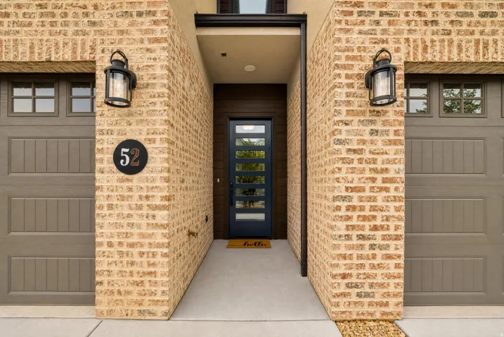 Brick exterior featuring a recessed entry, a contemporary dark-paneled front door with multiple glass inserts, dual garage doors with window panels, and two exterior light fixtures