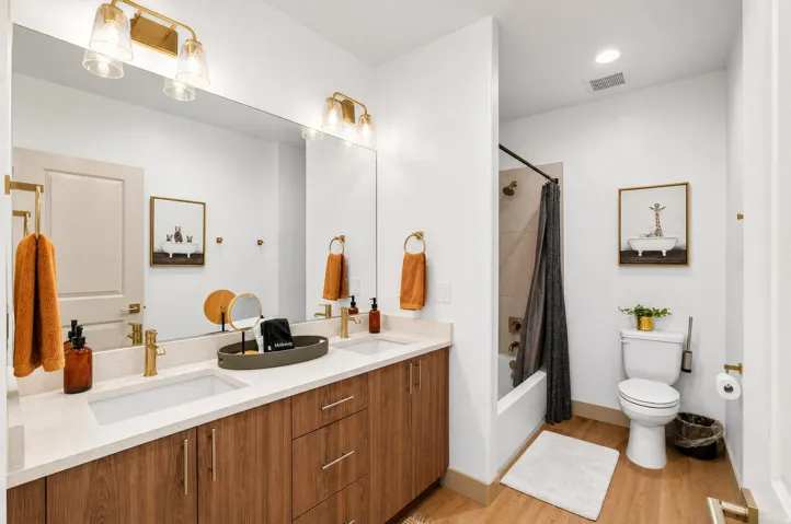 Dual vanity with wood-finish cabinetry, light-toned countertops, and gold-toned hardware