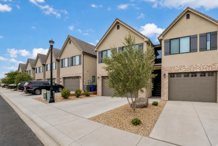 Townhome exterior featuring tan stucco, brick accents, and a gabled roofline