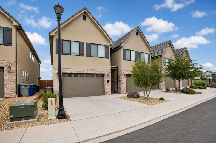 Stucco and brick facade with gabled roofs, multiple garages, and paved driveways