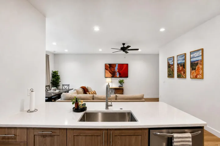 Kitchen island with a stainless steel sink, gooseneck faucet, light-toned countertop, and wood-finish cabinetry