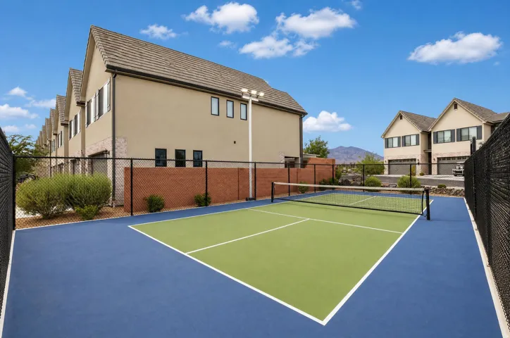 Outdoor sport court with a blue and green playing surface, surrounded by black chain-link fencing, and illuminated by an overhead light fixture
