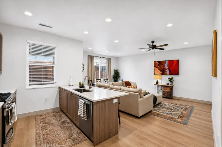 Kitchen island with integrated sink, wood-finish cabinetry, stainless steel dishwasher, and light-toned countertop