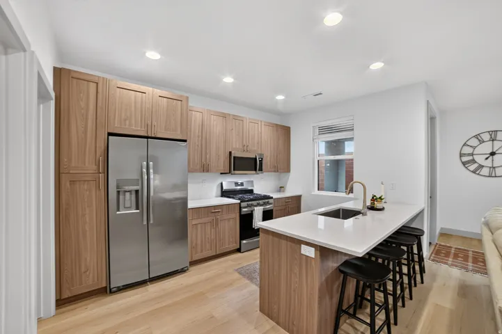 Modern kitchen featuring wood-finish cabinetry, stainless steel appliances, white countertops, and light wood-finish flooring