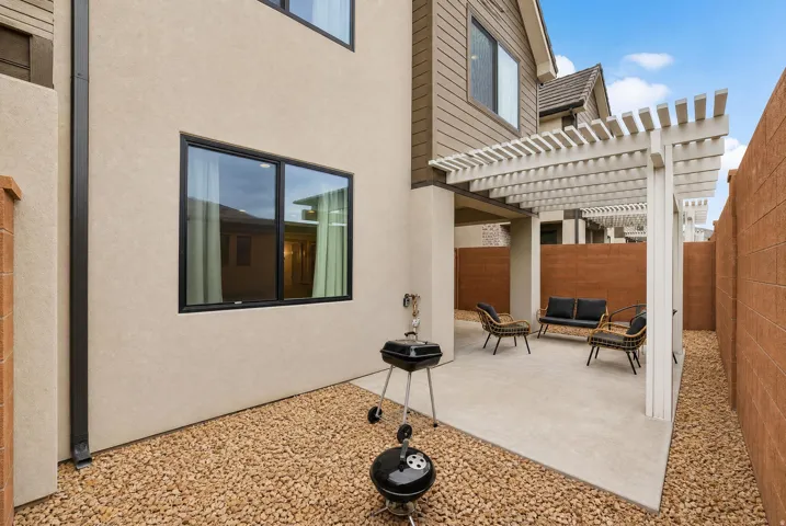 Backyard patio with a white pergola, concrete paving, and gravel landscaping
