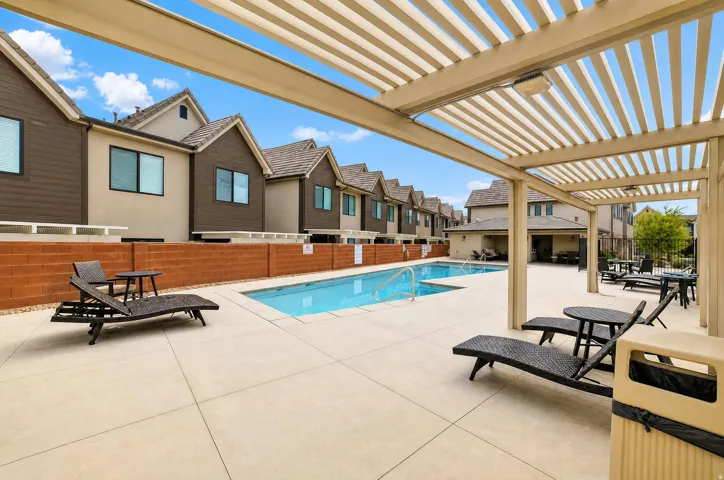 Community swimming pool with a concrete sundeck, a slatted pergola, and a brick privacy wall