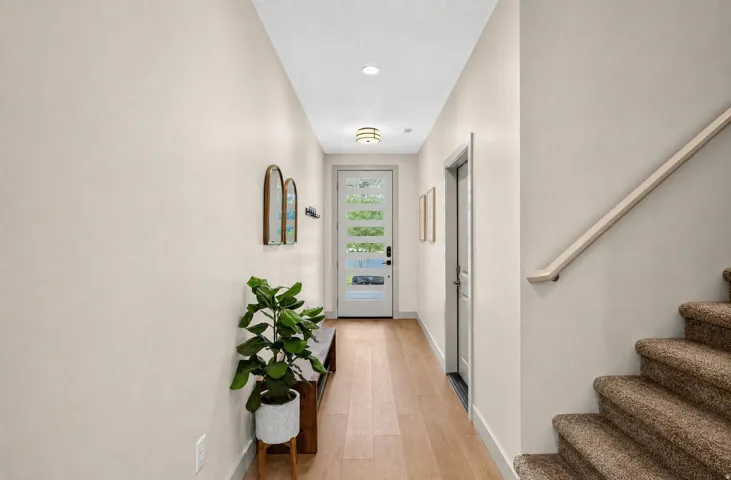 Light wood-finish flooring, white wall paint, recessed lighting, white interior door, and a staircase with carpeted treads