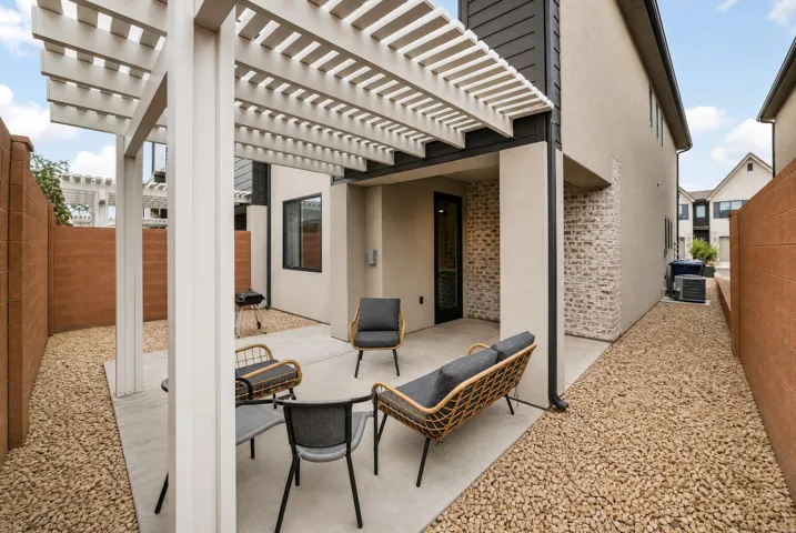 Private outdoor patio with a white pergola, concrete paving, a stone veneer accent wall, and gravel landscaping