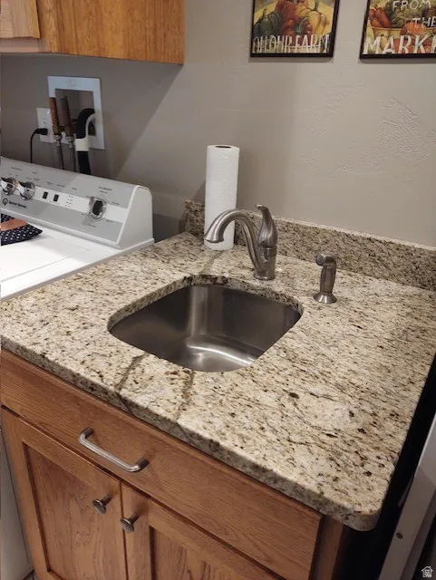 Laundry area featuring a stainless steel sink, granite countertop, and wood-finish cabinetry