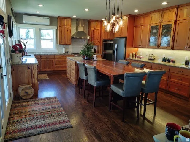 Wood-finish flooring, recessed lighting, wood cabinetry, built-in double oven, and a stainless steel range hood