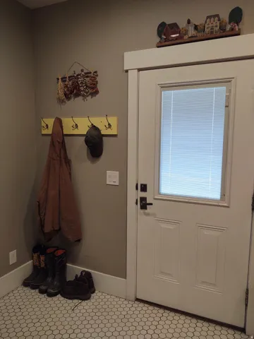 White paneled door with integrated blinds, wall-mounted coat rack, and hexagon tile flooring