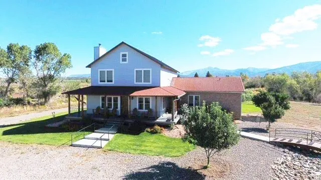 Charming two-story residence with a classic pitched roof and board-and-batten siding, situated on expansive grounds with mature landscape trees and open acreage