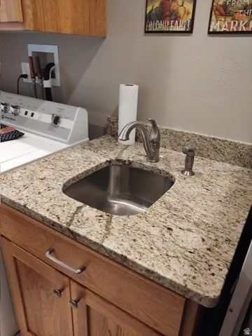 Laundry area featuring a stainless steel sink, granite countertop, and wood-finish cabinetry