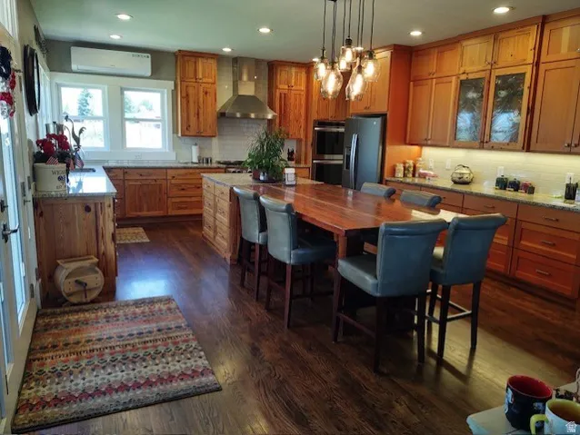 Wood-finish flooring, recessed lighting, wood cabinetry, built-in double oven, and a stainless steel range hood