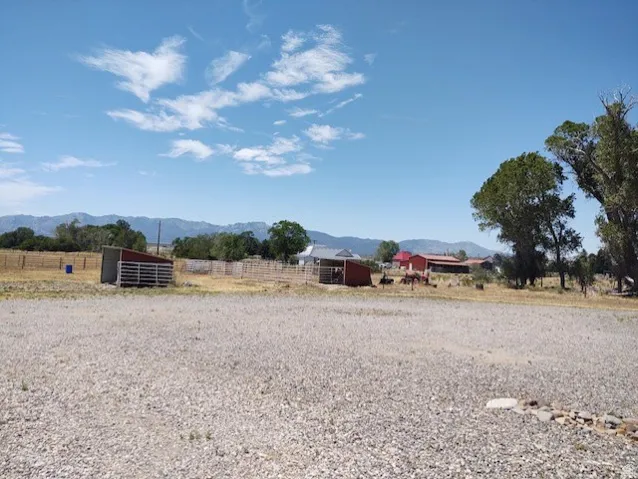 Expansive gravel area with distant mountain ranges, mature trees, and multiple outbuildings