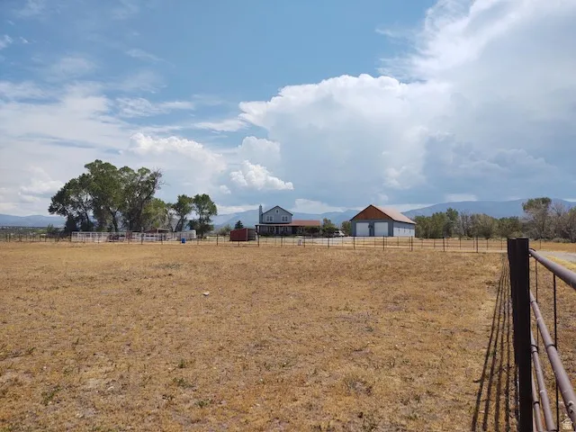 Expansive land with distant mountains, featuring a multi-story residence, a large barn structure, and perimeter fencing