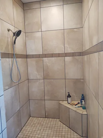 Walk-in shower with large-format wall tiling, a decorative tile accent band, a built-in corner bench, and mosaic tile flooring