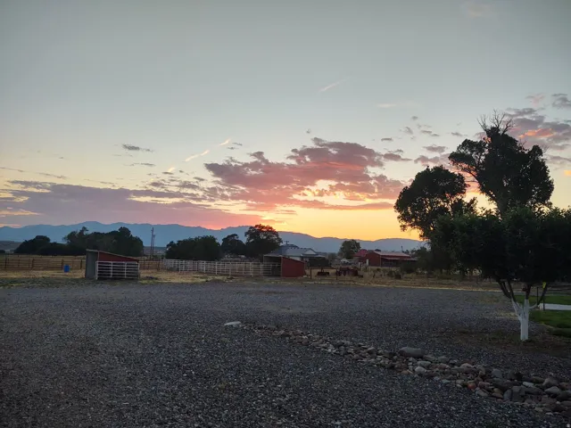 Expansive gravel area with natural stone border, mature trees, and outbuildings, all framed by distant mountains