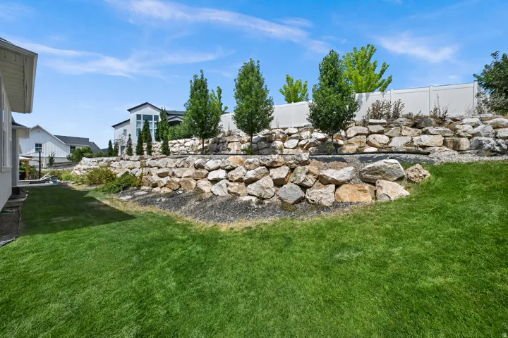 Expansive lawn with multi-tiered rock retaining walls, mature trees, and a privacy fence