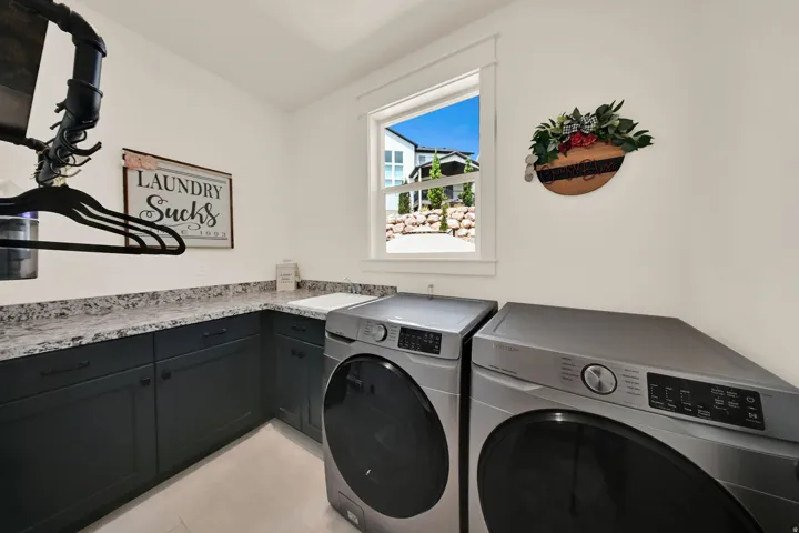 Laundry area featuring dark cabinetry, speckled countertops, a built-in sink, and a window with white trim