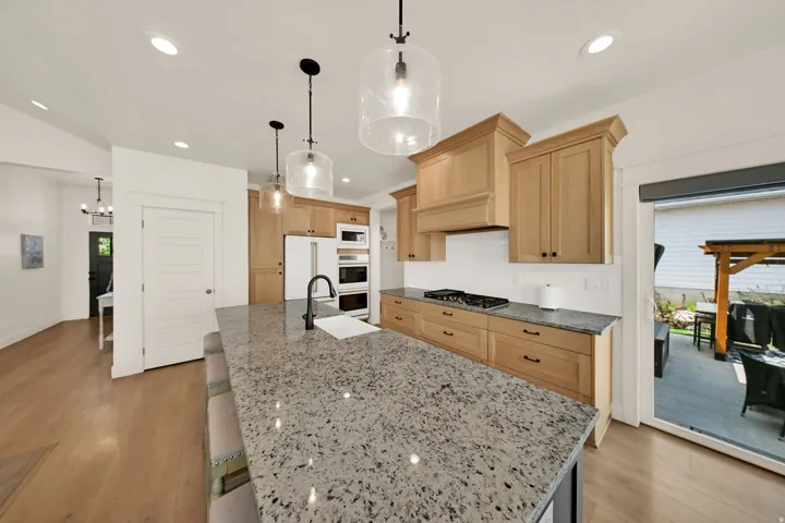 Kitchen featuring natural wood cabinetry, light-toned wood-finish flooring, a spacious island with a stone countertop, a built-in gas range, and recessed lighting