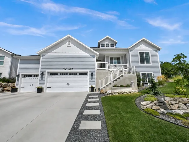 Gable roofline, light-toned siding, attached two-car garage, concrete driveway, and tiered landscaping