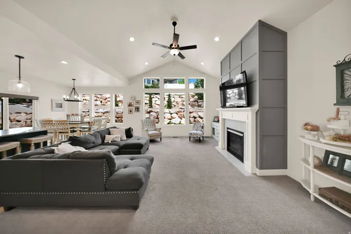 Vaulted ceiling, recessed lighting, ceiling fan, carpet flooring, and a fireplace with a white mantel and board-and-batten surround