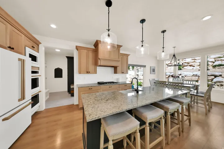 Open-concept kitchen with wood-finish flooring, light wood cabinetry, white subway tile backsplash, and a large central island featuring a stone-finish countertop