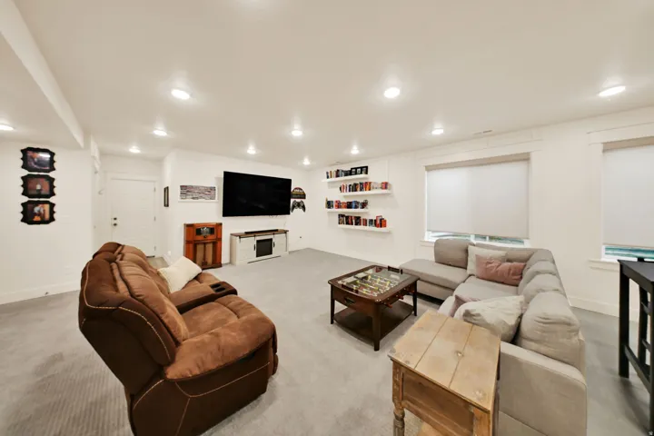 Recessed lighting throughout, two windows with roller shades, built-in shelving, white paneled door, and light-toned carpet