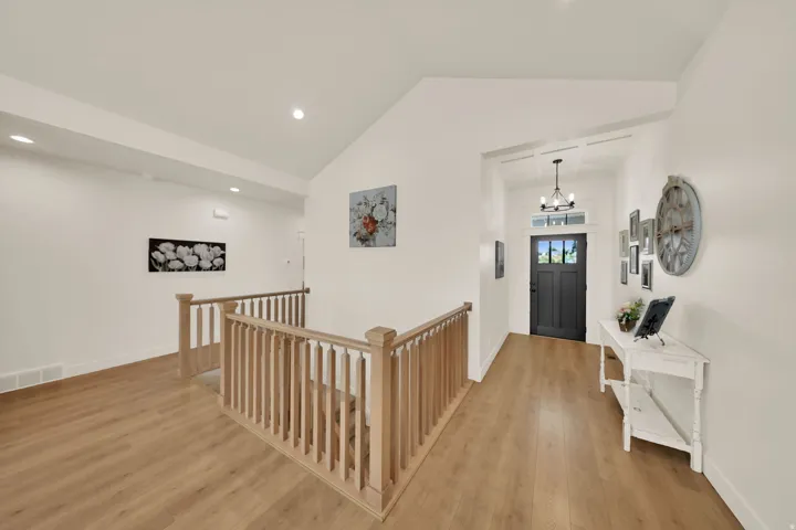 Hardwood-style flooring throughout, light wood-finish railings, recessed lighting, vaulted ceilings, and a dark-paneled front door with transom window