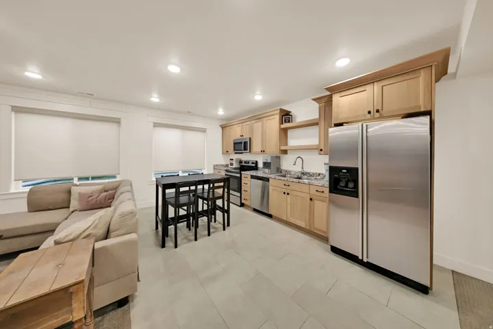 Integrated kitchen and living area featuring light wood cabinetry, stainless steel appliances, a bar-height dining area, recessed lighting, and tile flooring