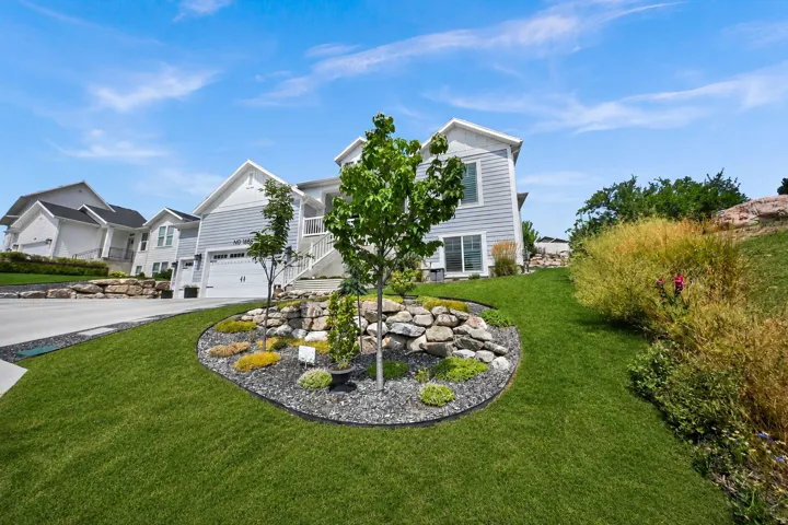 Contemporary exterior siding, attached garage, concrete driveway, stone retaining walls, and landscaped yard