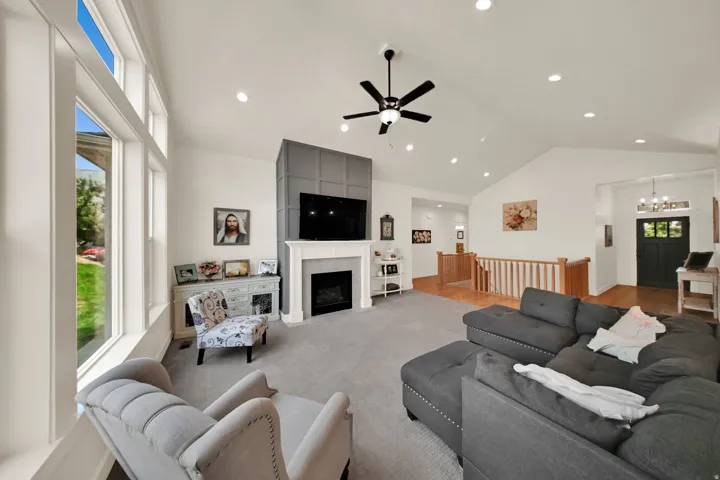 Vaulted ceilings with recessed lighting, full-height paneled accent wall, gas fireplace, large windows, and hardwood-finish flooring