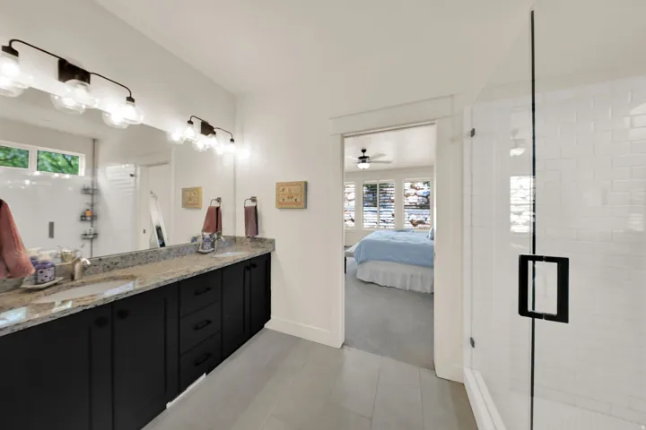 Dual vanity with stone countertop, large wall-mounted mirror, and glass-enclosed shower with subway tile