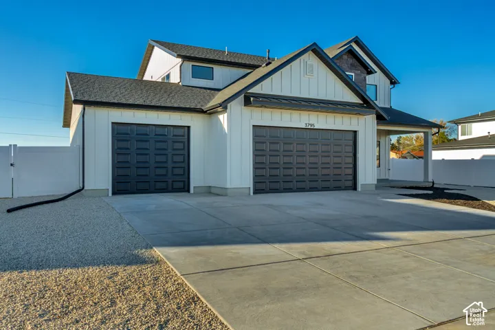 Modern exterior featuring white board and batten siding, dark shingle roofing, and a two-car garage with paneled doors