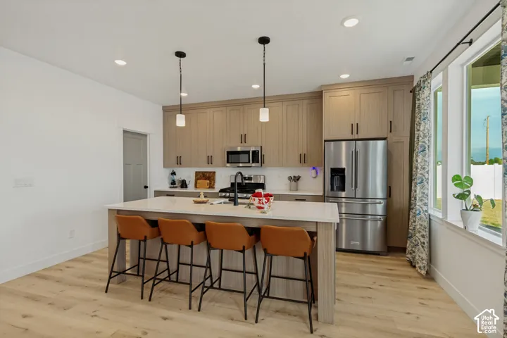 Kitchen featuring an island with built-in seating, stainless steel appliances, light wood-finish cabinetry, recessed lighting, and wood-finish flooring