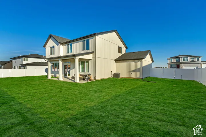 Expansive grassy backyard featuring a covered patio, vinyl fencing, and a two-story exterior with vertical siding