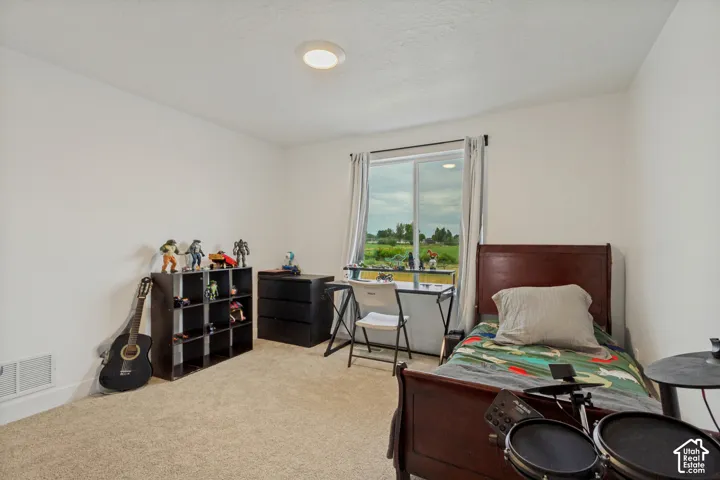 Versatile bedroom with plush carpet flooring, abundant natural light from large glass sliding doors, recessed ceiling lighting, and ample space for multiple functional zones including work and hobby areas