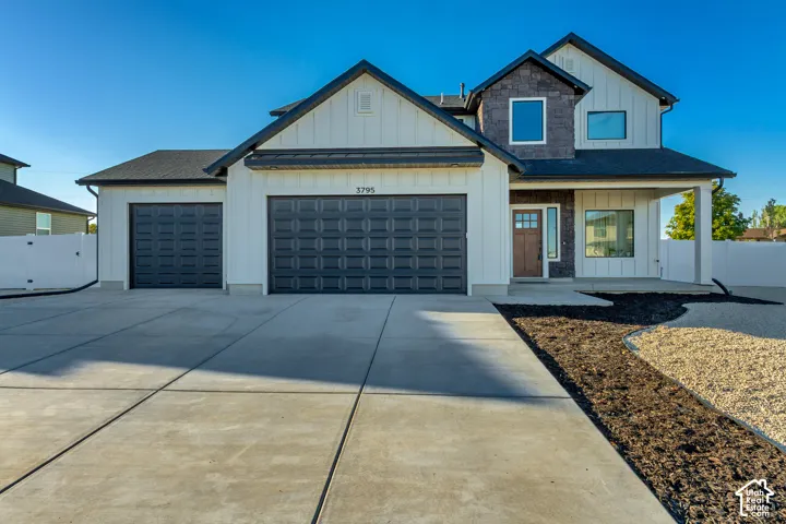 Board and batten siding with stone accents, covered front entry, two-car garage, and concrete driveway